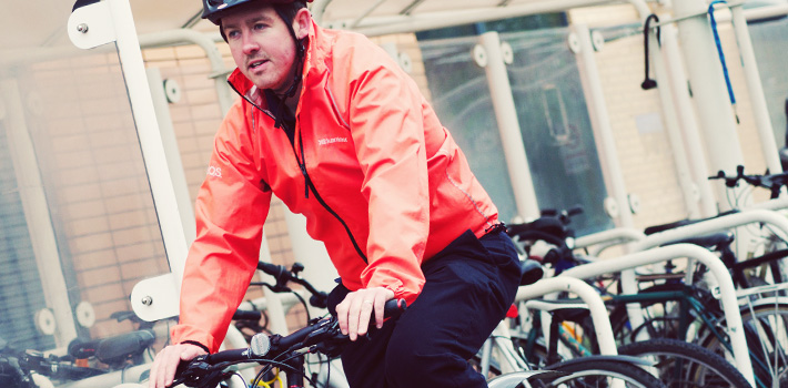 Cyclist in orange jacket arriving at bike rack